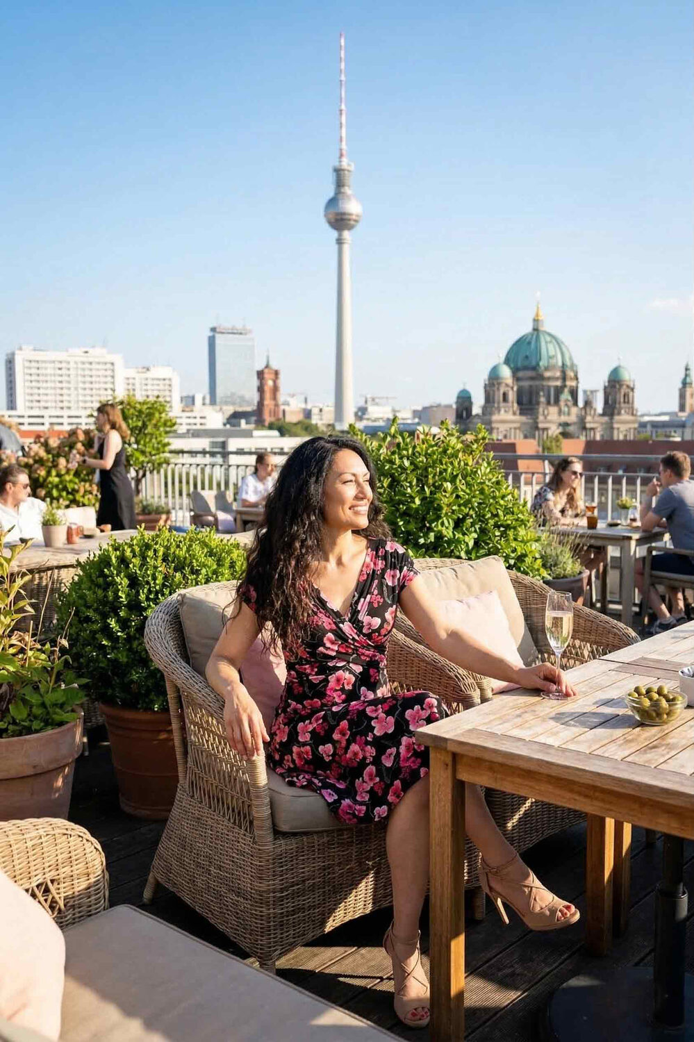 Frau sitzt auf einer Terrasse und trägt ein kurzes, geblümtes Sommerkleid mit schwingendem Rock und einem Oberteil in Wickeloptik und V-Ausschnitt.