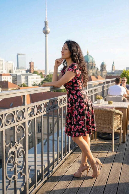 Frau steht auf einer Terrasse und trägt ein kurzes, geblümtes Sommerkleid mit schwingendem Rock und einem Oberteil in Wickeloptik.